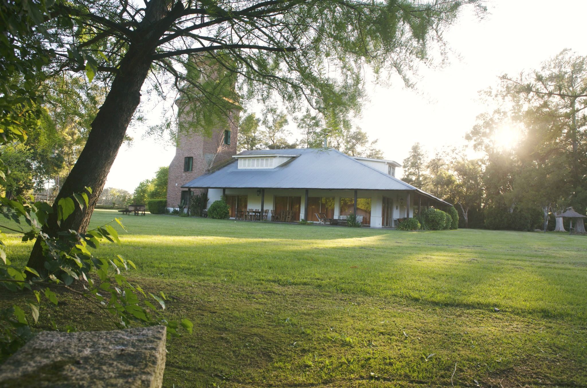 La casa y la torre al amanecer, con el sol entre los árboles