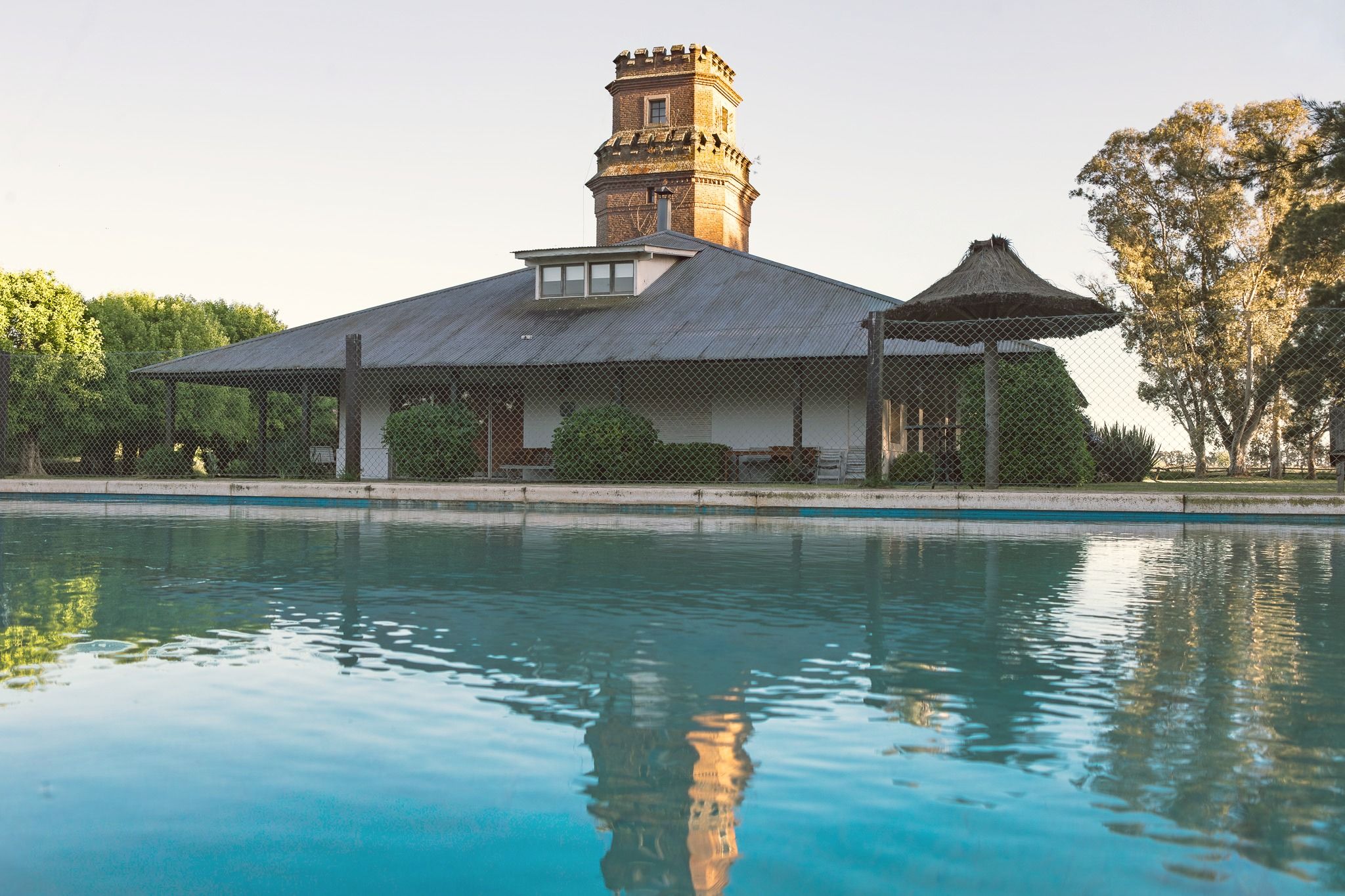 La pileta con la casa principal y la torre de ladrillo reflejadas en el agua